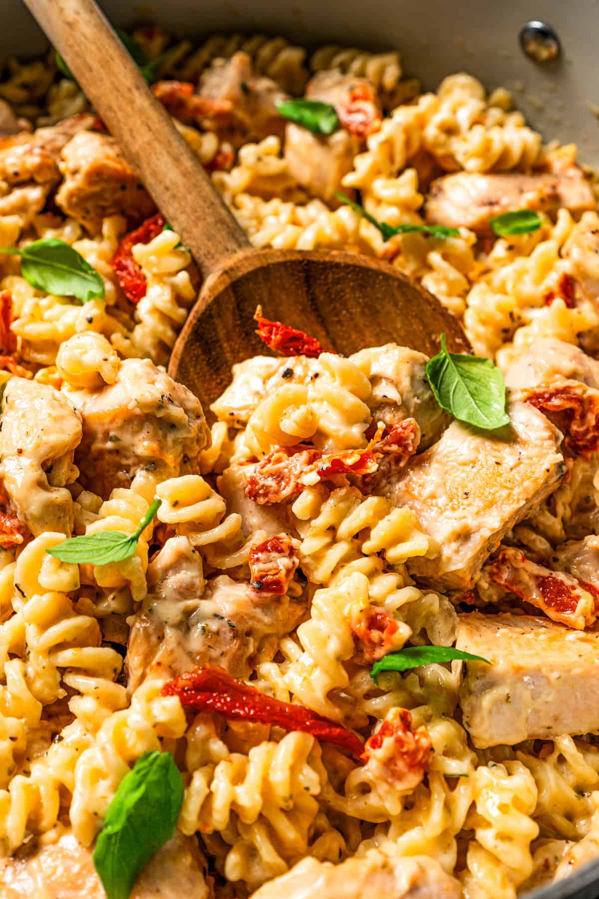 Close up overhead view of marry me chicken pasta in a skillet with a wooden spoon stirring through it.