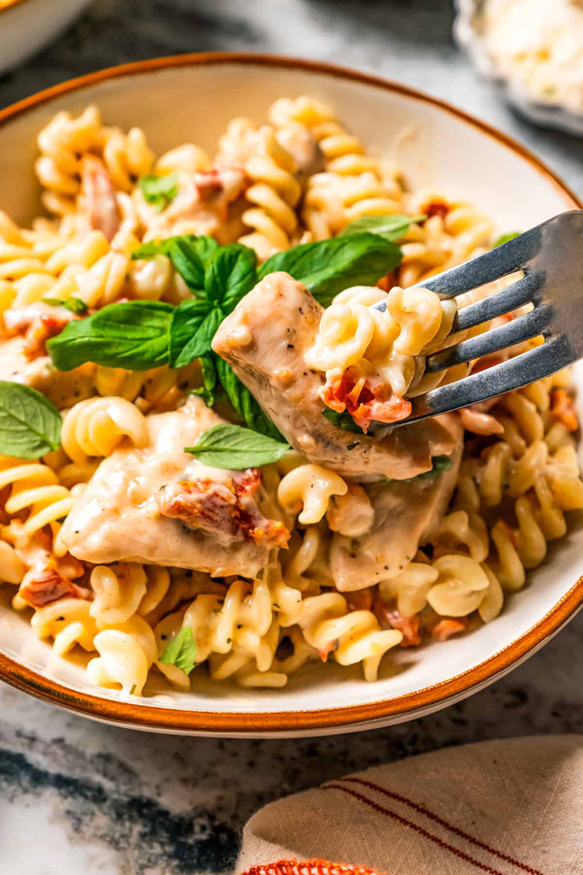 A fork picking up a bite of marry me chicken pasta from a bowl.