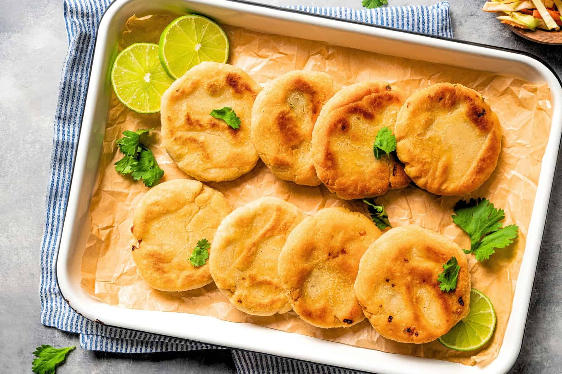 This Salvadoran pupusas recipe makes crispy masa cakes stuffed with refried beans, pickled jalapeños, and melted cheese. Served with curtido! Pupusas arranged in rows on a tray garnished with lime slices.