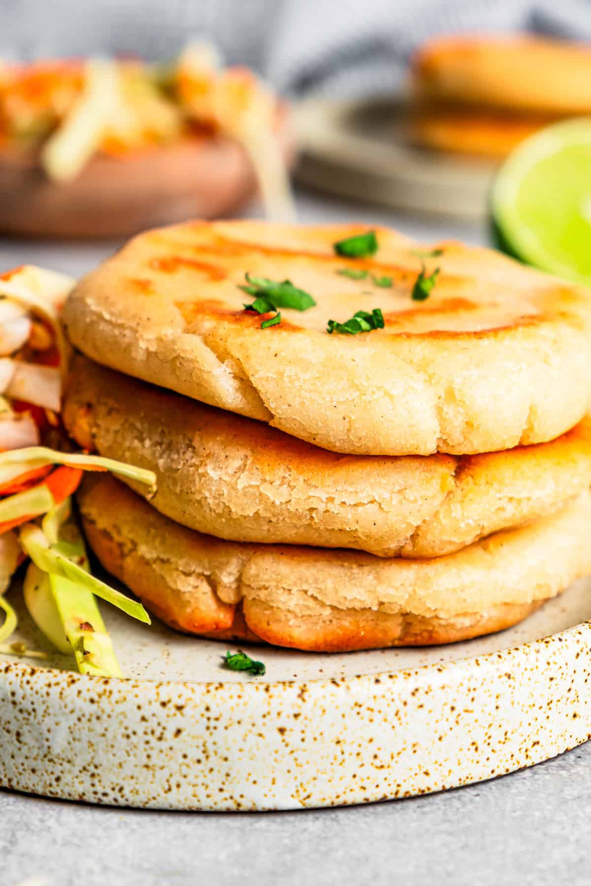 Pupusas stacked next to curtido on a stoneware plate.