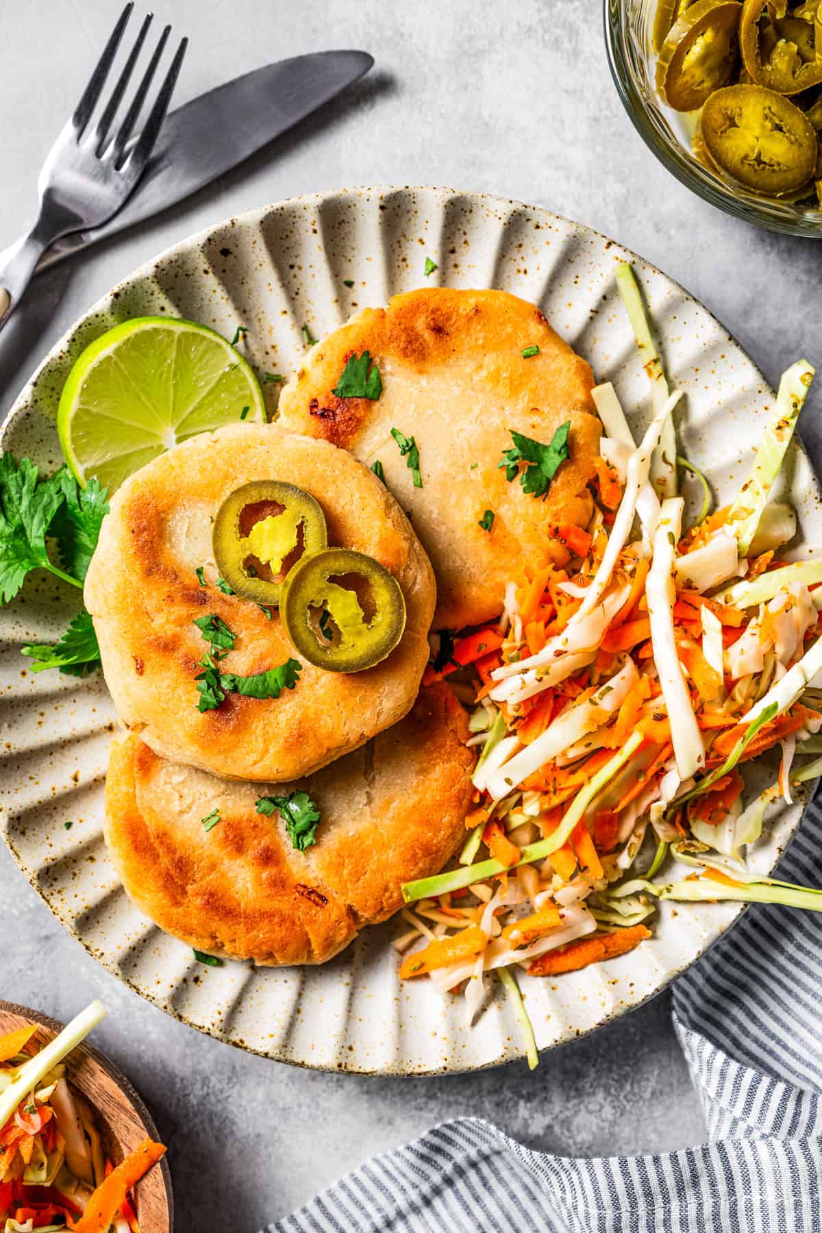 Overhead view of pupusas with curtido on a plate garnished with jalapeño and lime slices.