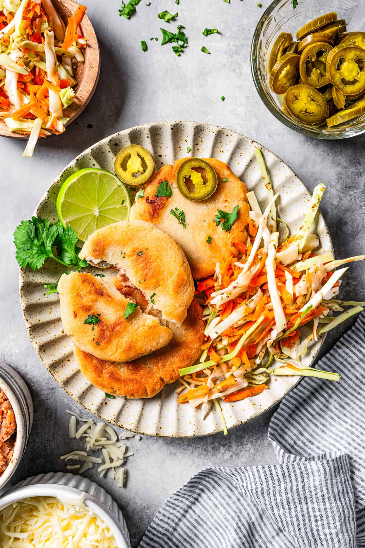 Overhead view of pupusas with curtido on a plate garnished with jalapeño and lime slices.