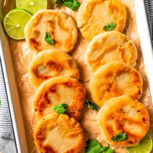 Pupusas arranged in rows on a tray garnished with lime slices.