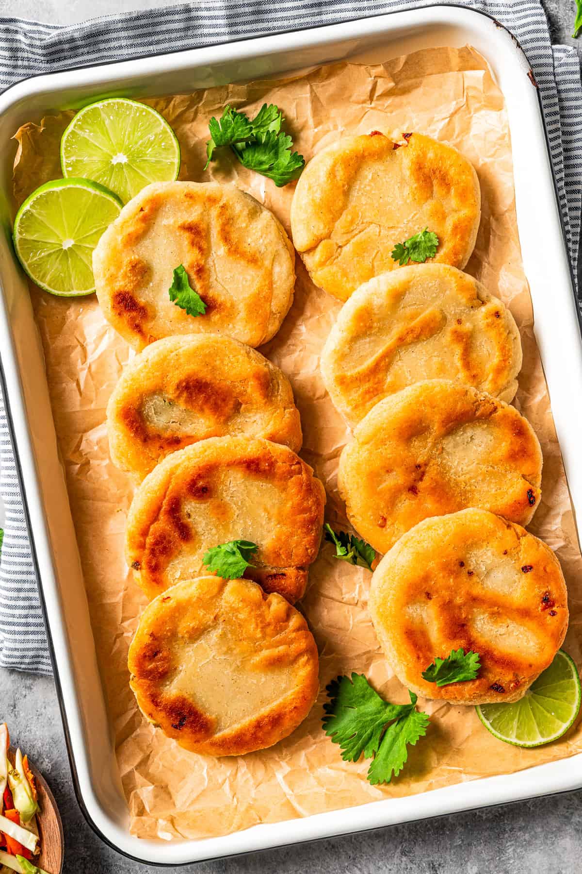 Pupusas arranged in rows on a tray garnished with lime slices.