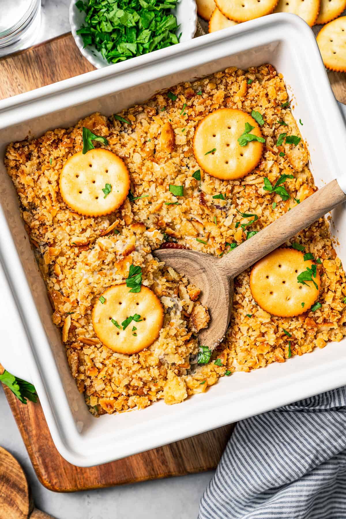 Overhead view of a Ritz chicken casserole topped with Ritz crackers in a baking dish with a wooden spoon scooping out the food.