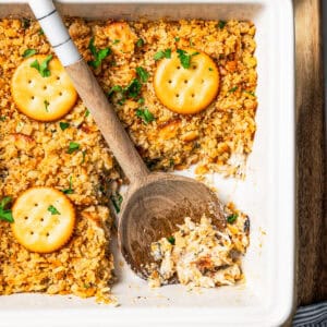 Chicken casserole topped with Ritz crackers in a baking dish with wooden spoon resting in an open serving.