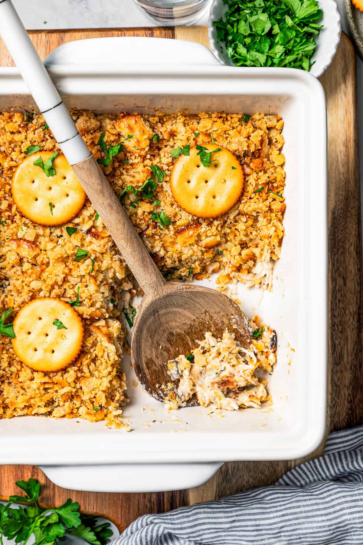 Chicken casserole topped with Ritz crackers in a baking dish with wooden spoon resting in an open serving.