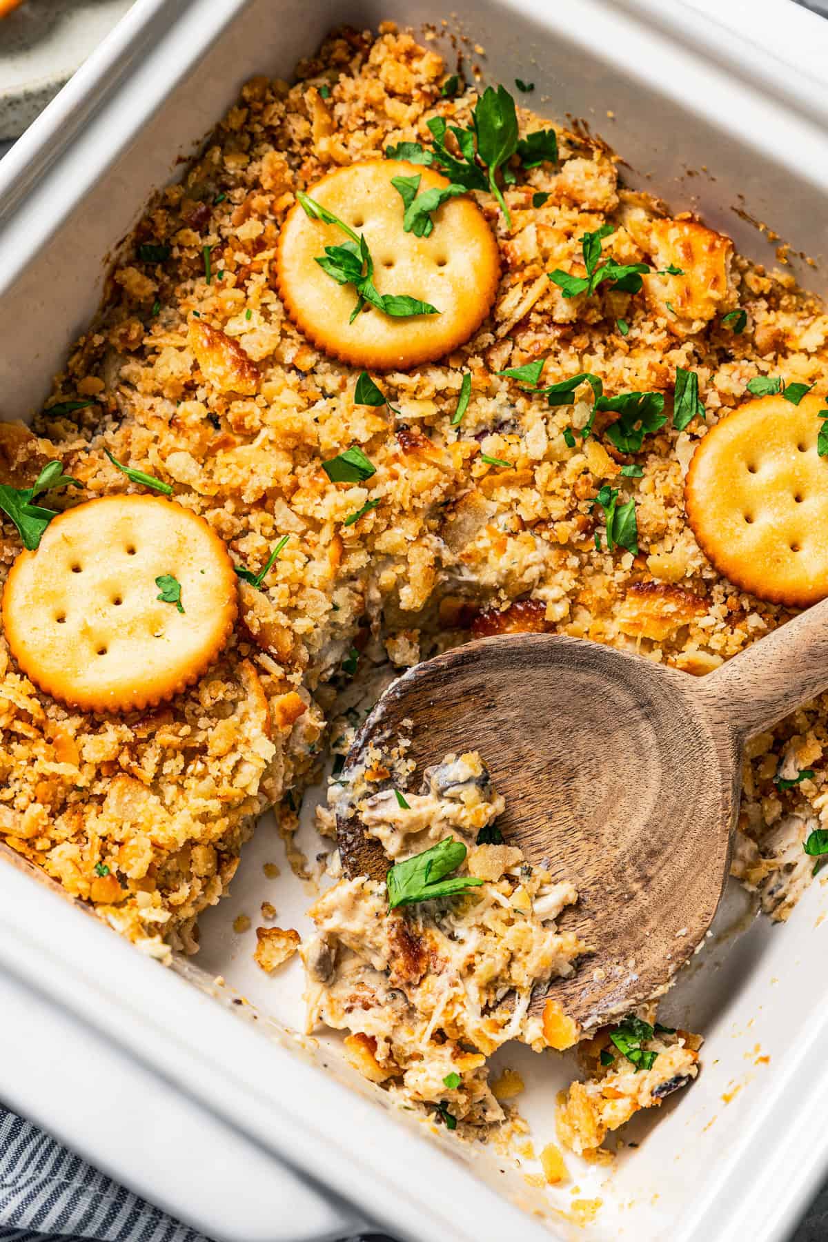 Ritz chicken casserole in a baking dish with wooden spoon stirring through it.