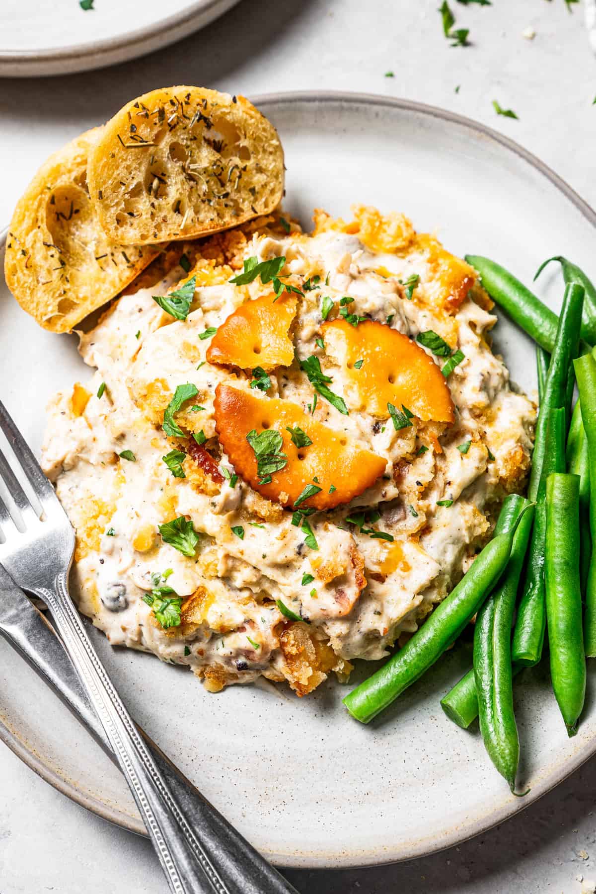 A serving of Ritz chicken casserole next to bread slices and green beans on a plate.