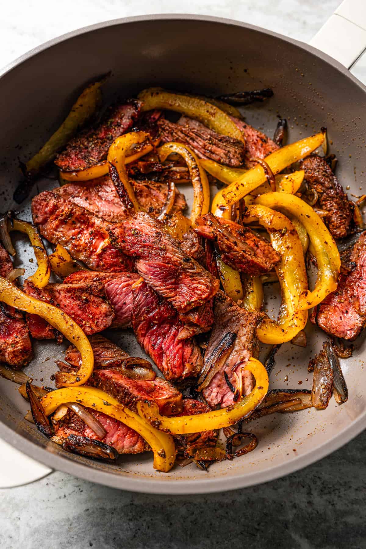 Sautéed sliced steak and yellow peppers in a skillet.