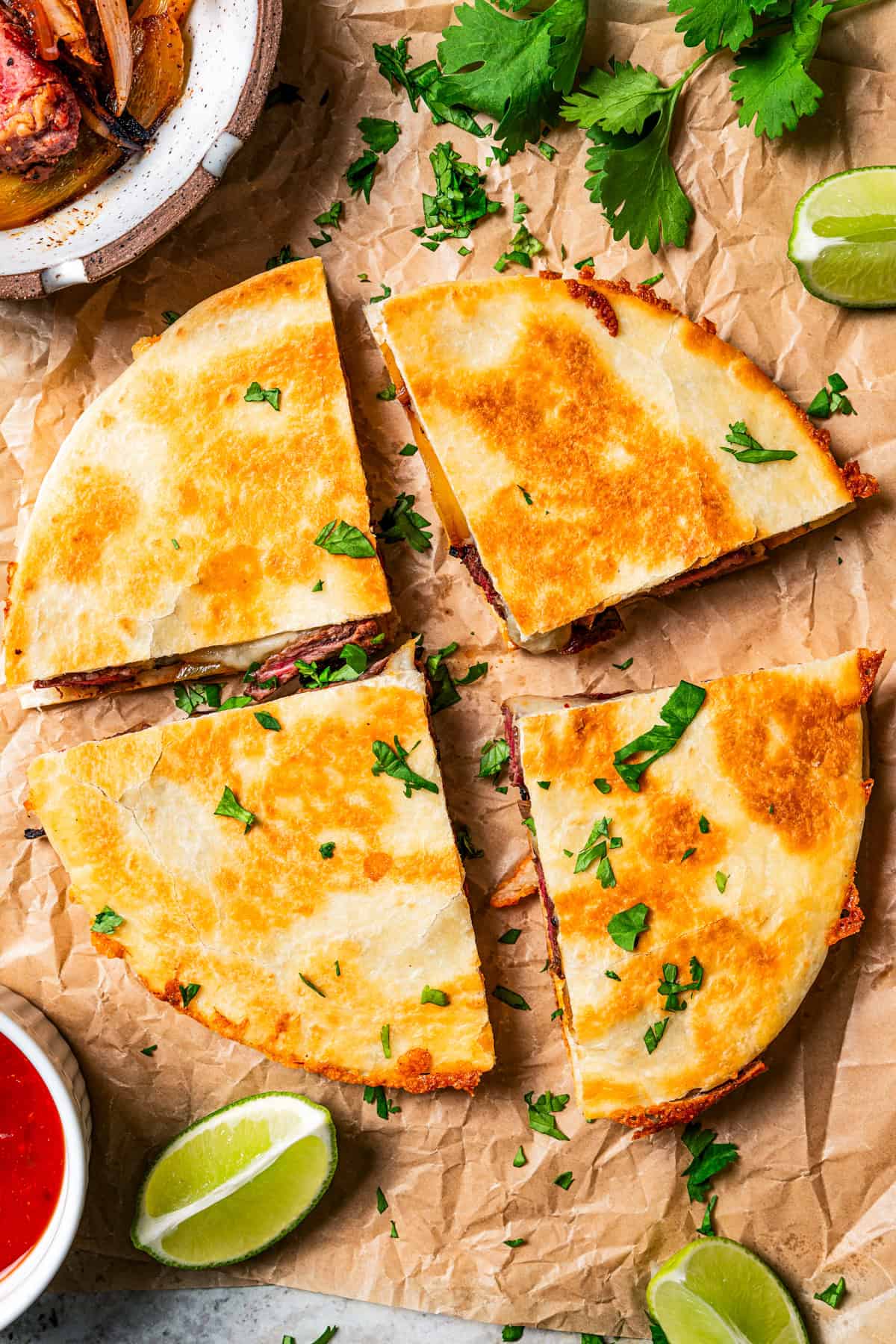 Large quesadilla sliced into quarters on a sheet of parchment paper.