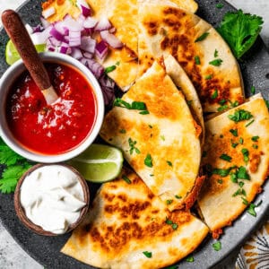 Steak quesadillas arranged around bowls of salsa and sour cream on a large serving plate.