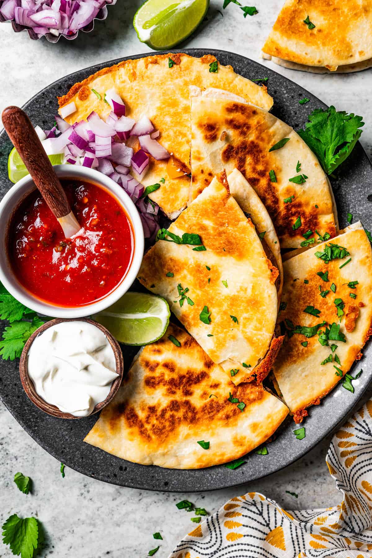 Steak quesadillas arranged around bowls of salsa and sour cream on a large serving plate.