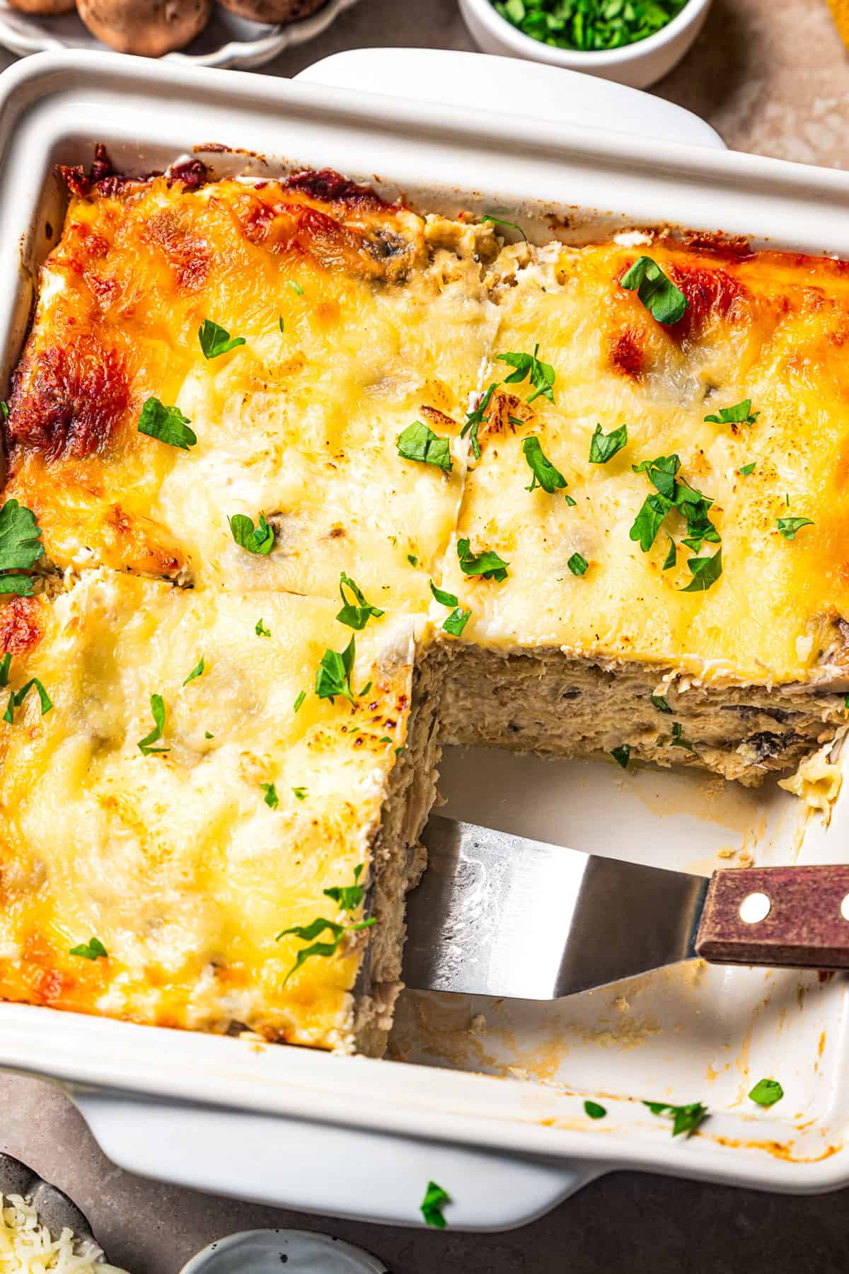 Overhead view of white chicken lasagna in a ceramic casserole dish, with a spatula resting in an open space where a slice used to be.