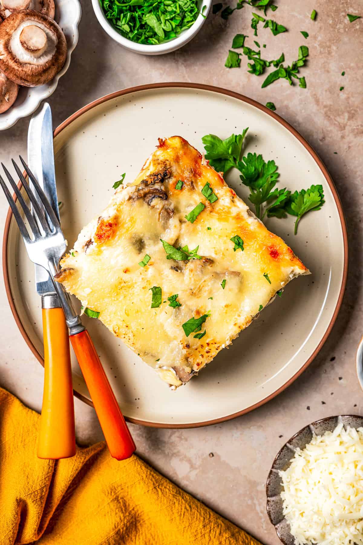 A slice of white chicken lasagna on a stoneware plate next to a fork and knife.