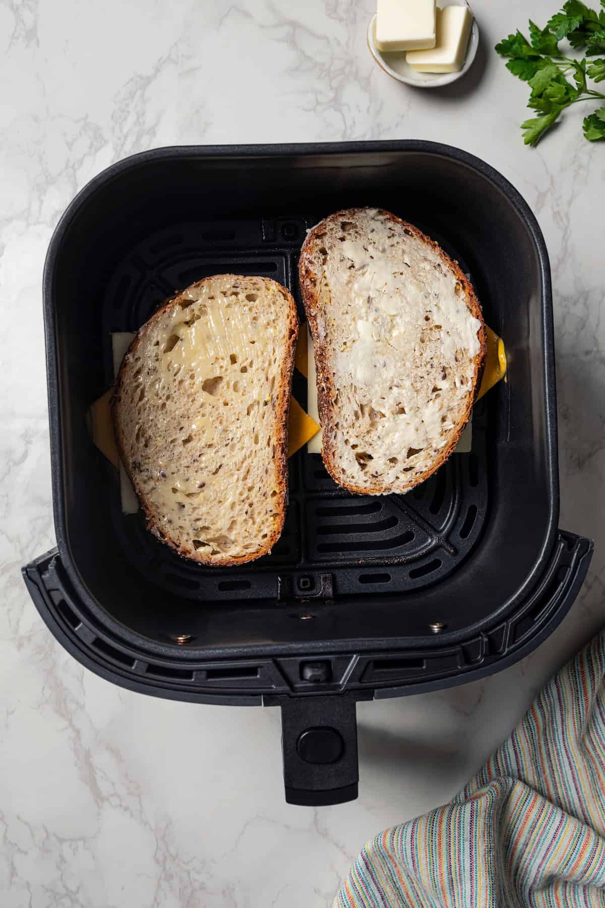 Two assembled grilled cheese sandwiches inside the air fryer basket.