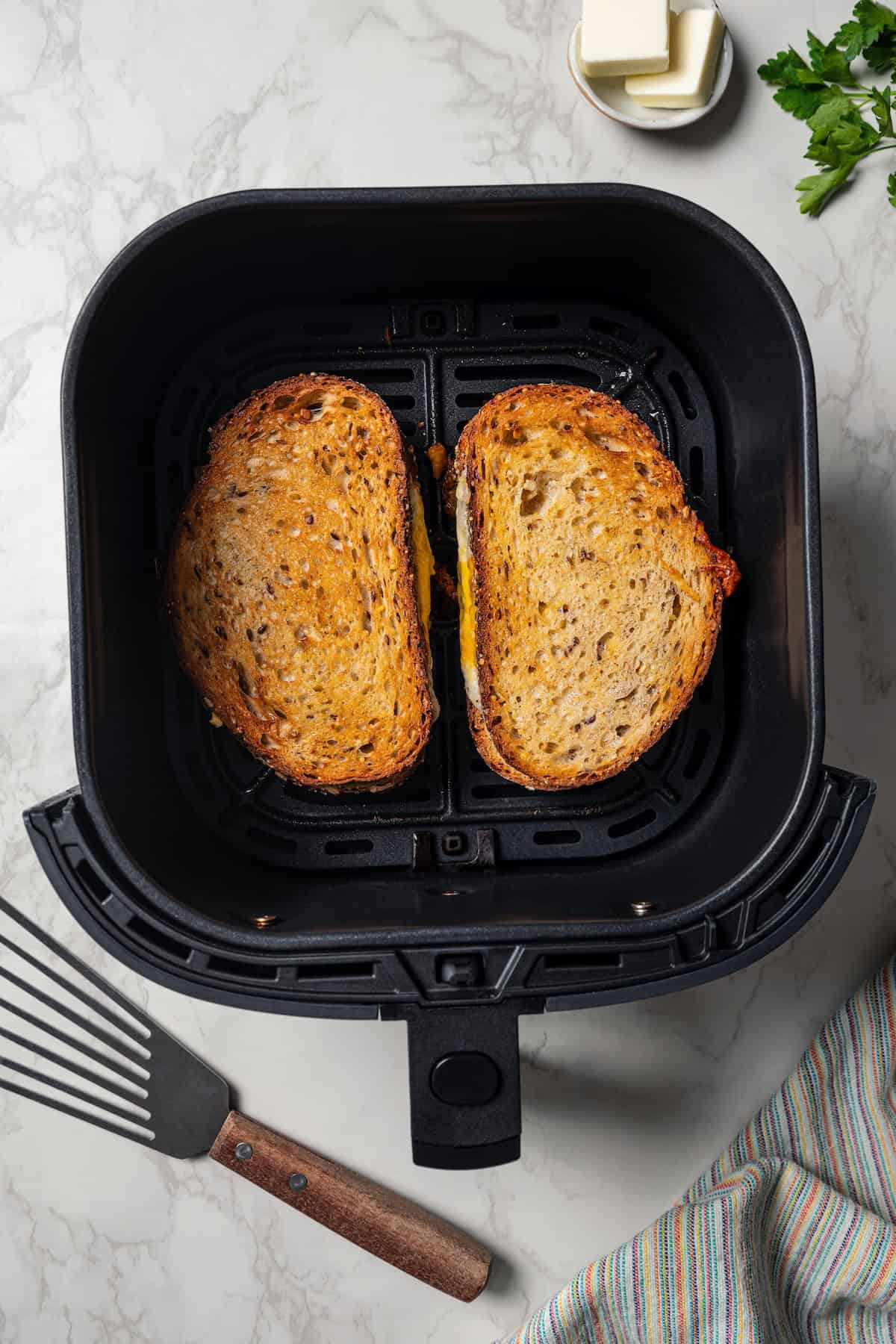 Two toasted grilled cheese sandwiches inside the air fryer basket.