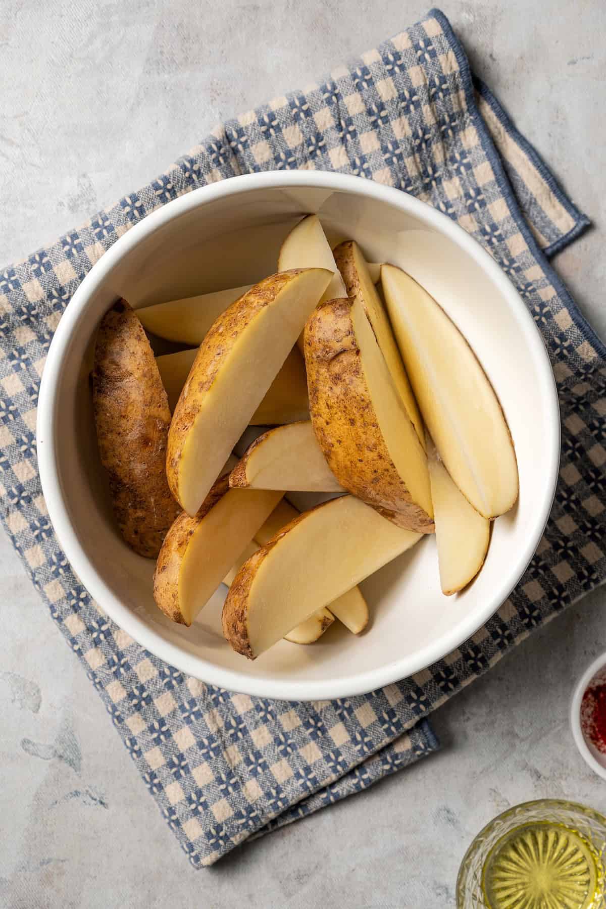 Russet potatoes cut into wedges in a white bowl.