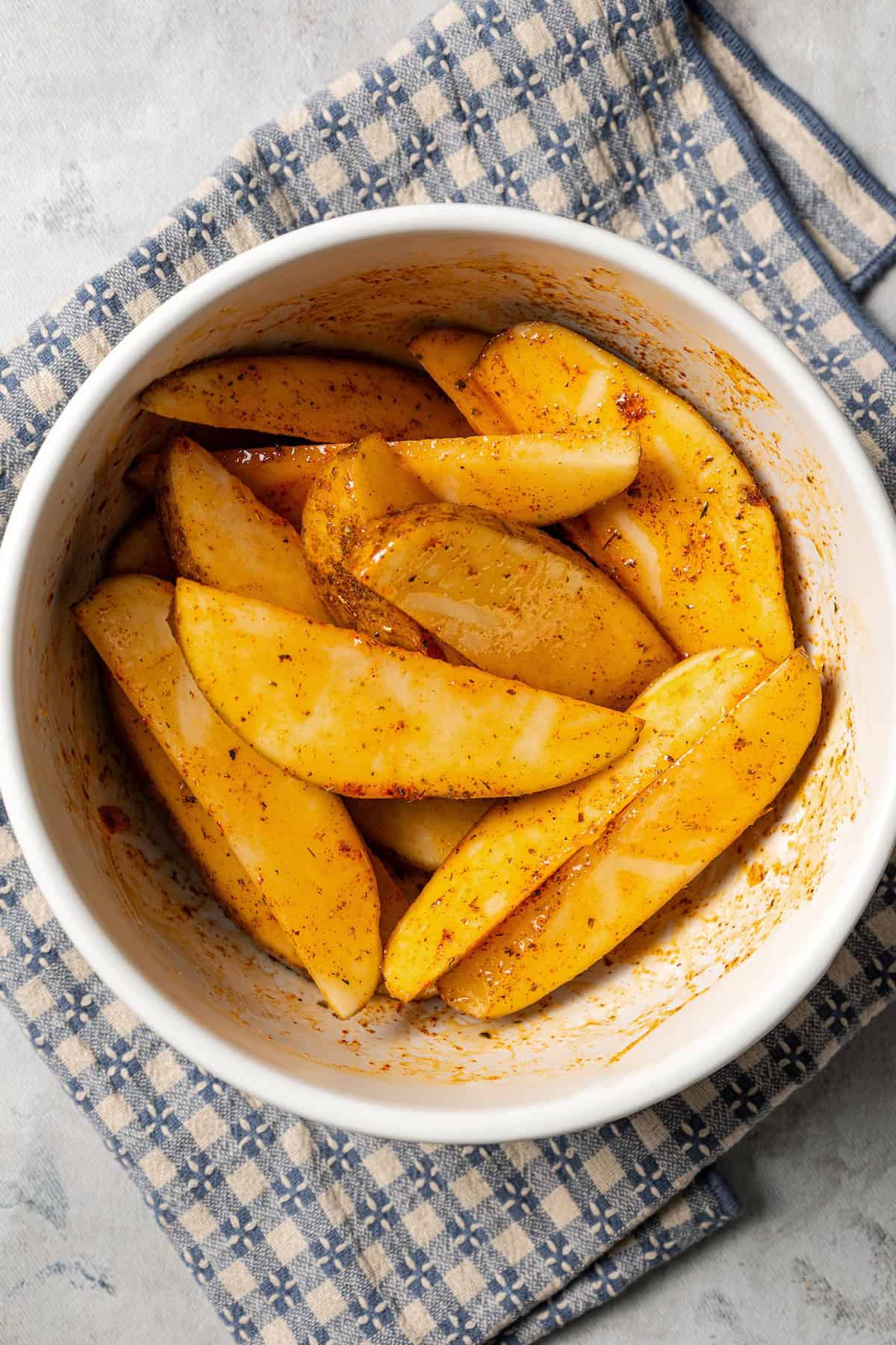 Seasoned potato wedges in a white bowl.