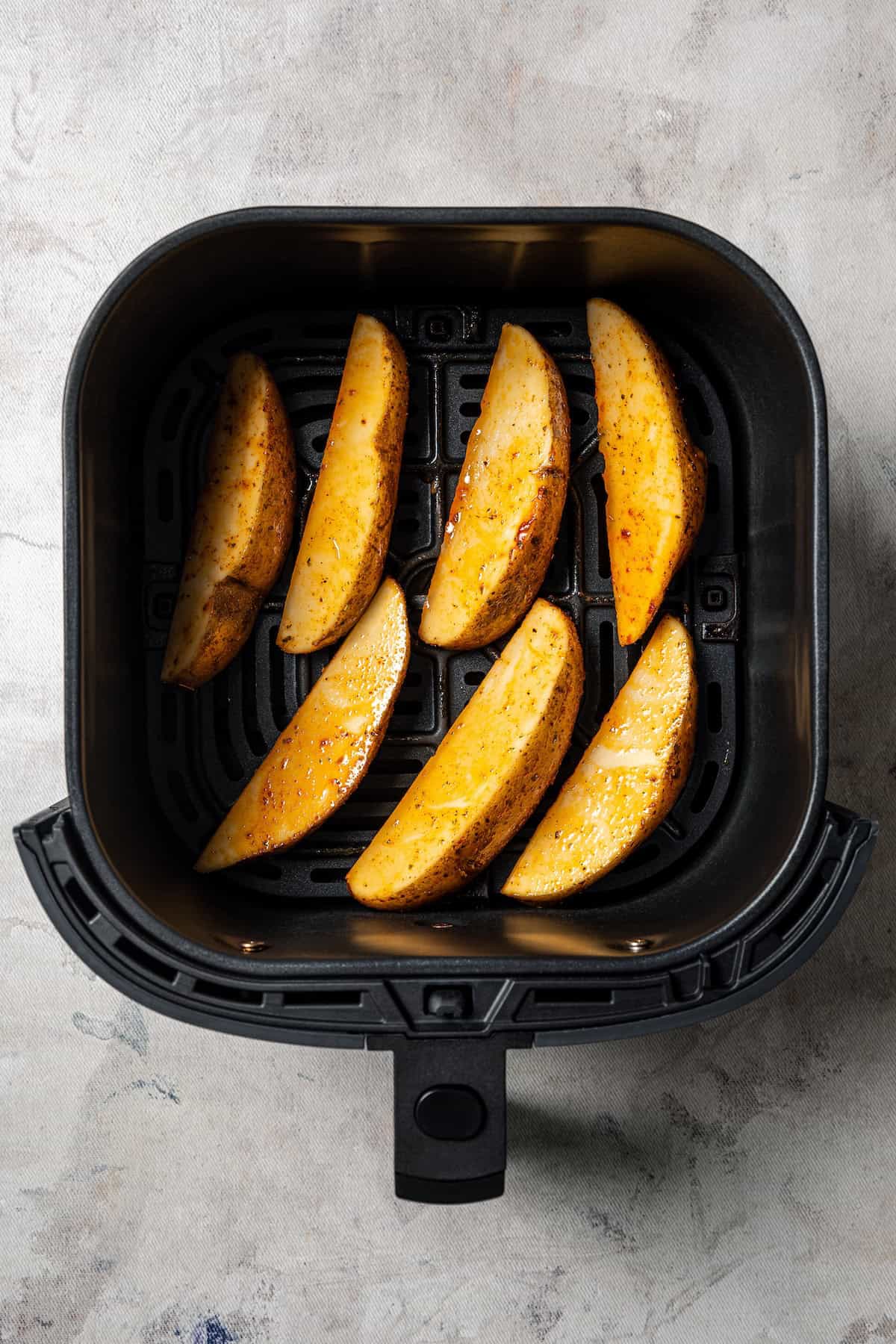 Seasoned potato wedges added to the air fryer basket.