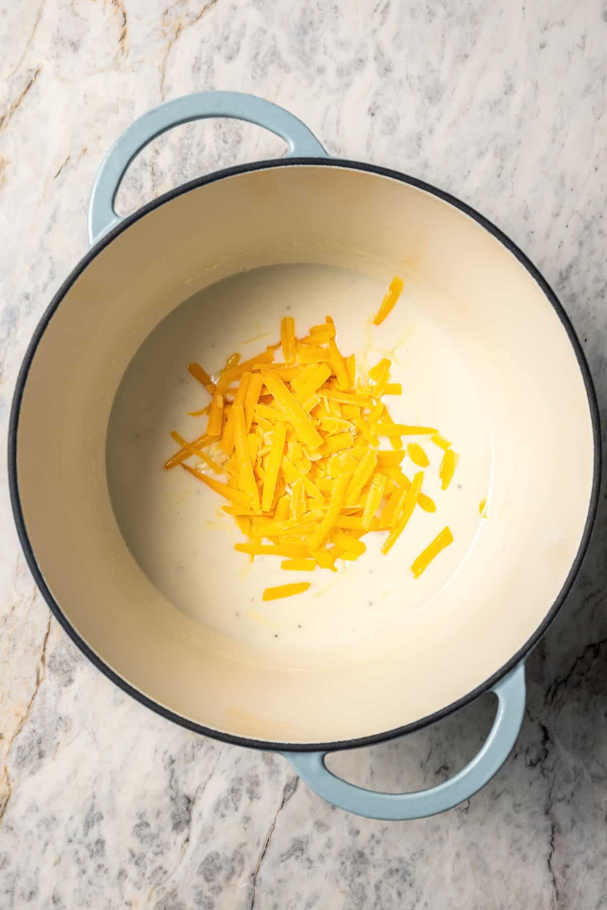 Shredded cheese added to a roux of butter and flour in a pot.