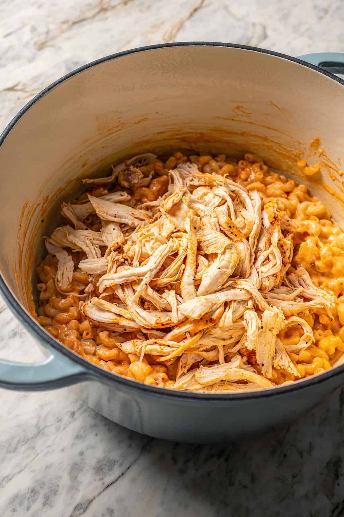 Shredded chicken added to buffalo mac and cheese in a large pot.