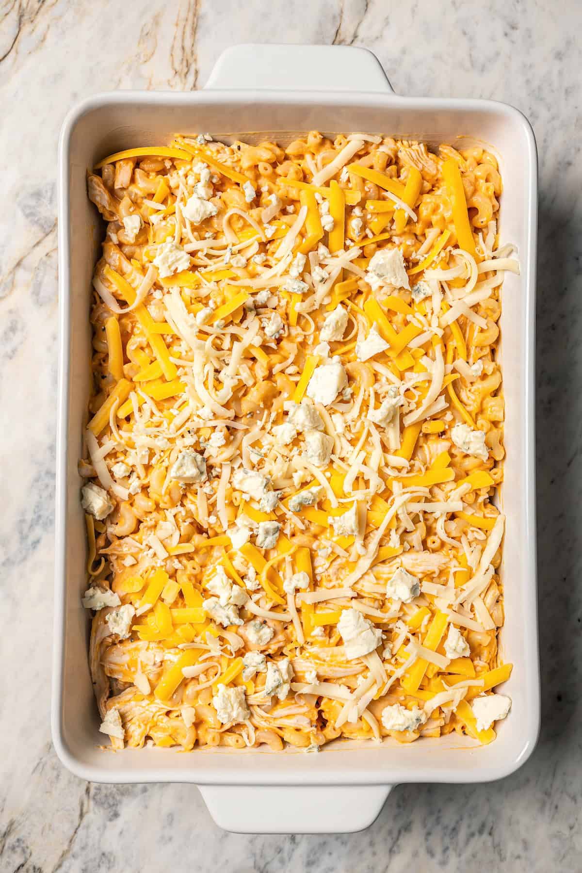 Buffalo mac and cheese in a baking dish topped with shredded cheese and crumbled gorgonzola.