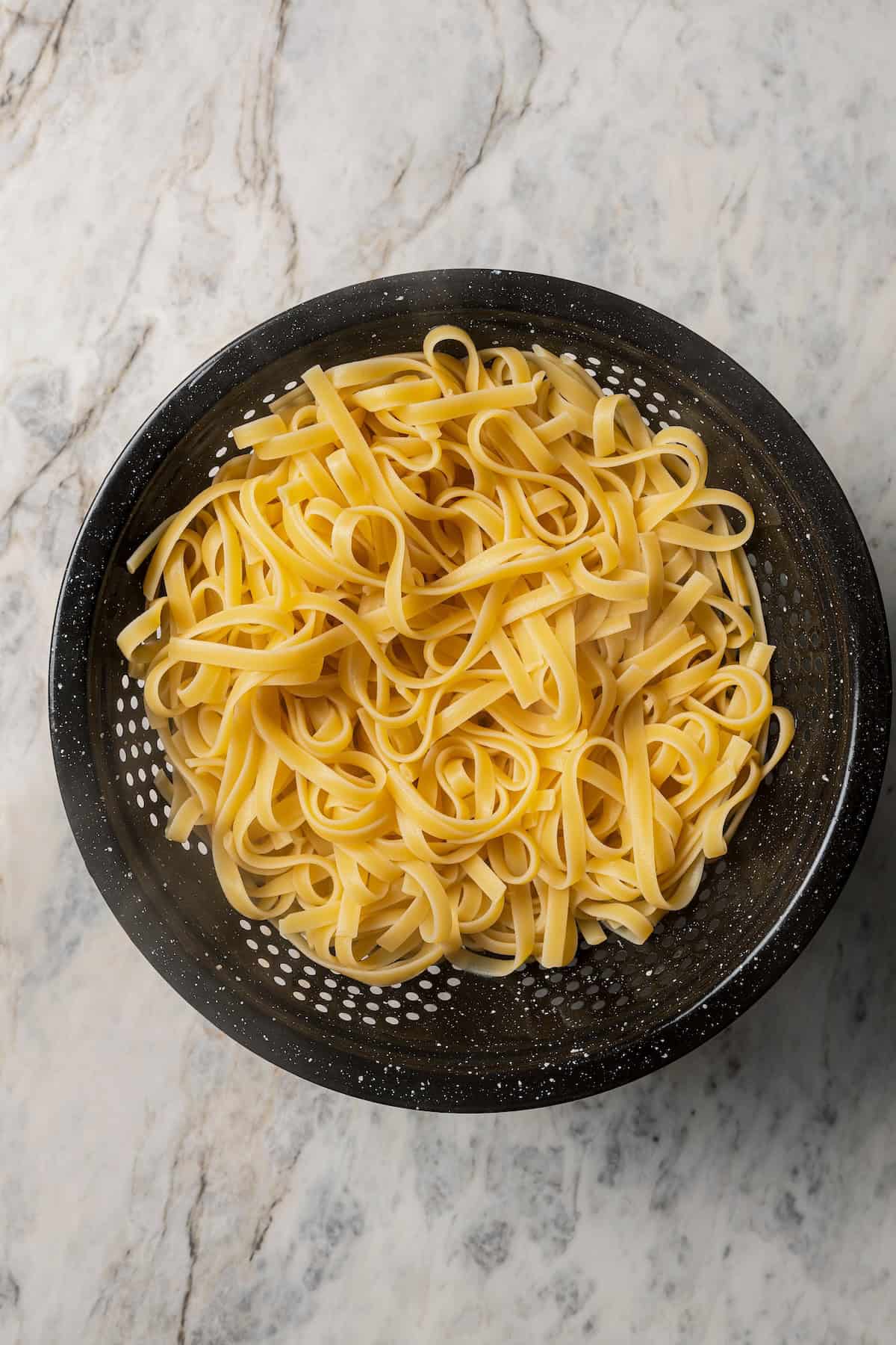 Cooked fettuccine pasta in a black colander.