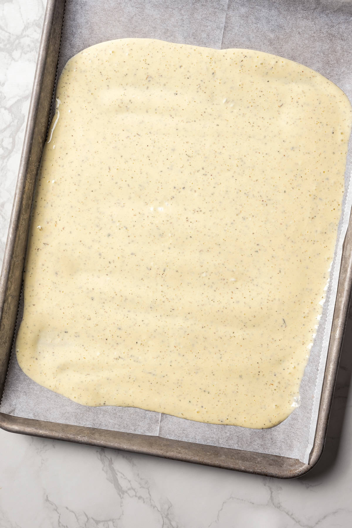 Cottage cheese flatbread batter spread into a large rectangle on a parchment-lined baking sheet.