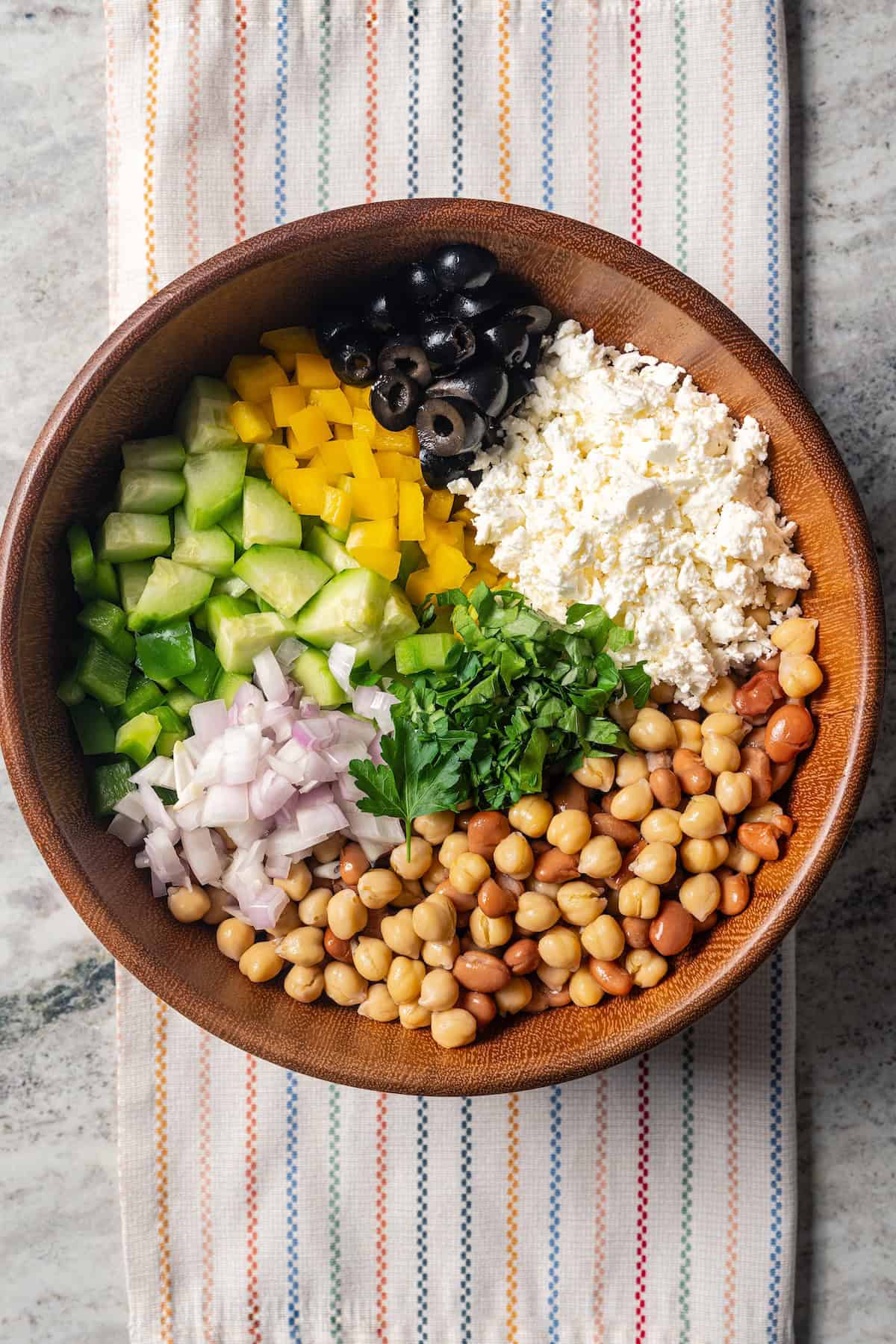 Dense bean salad ingredients combined in a large wooden bowl.