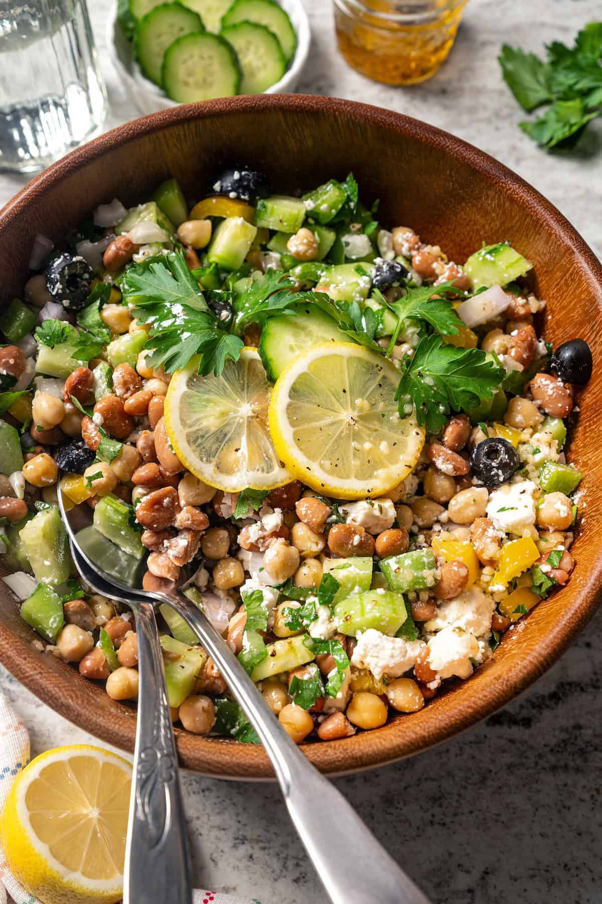 Overhead view of dense bean salad garnished with lemon slices in a wooden bowl with a pair of salad tongs.