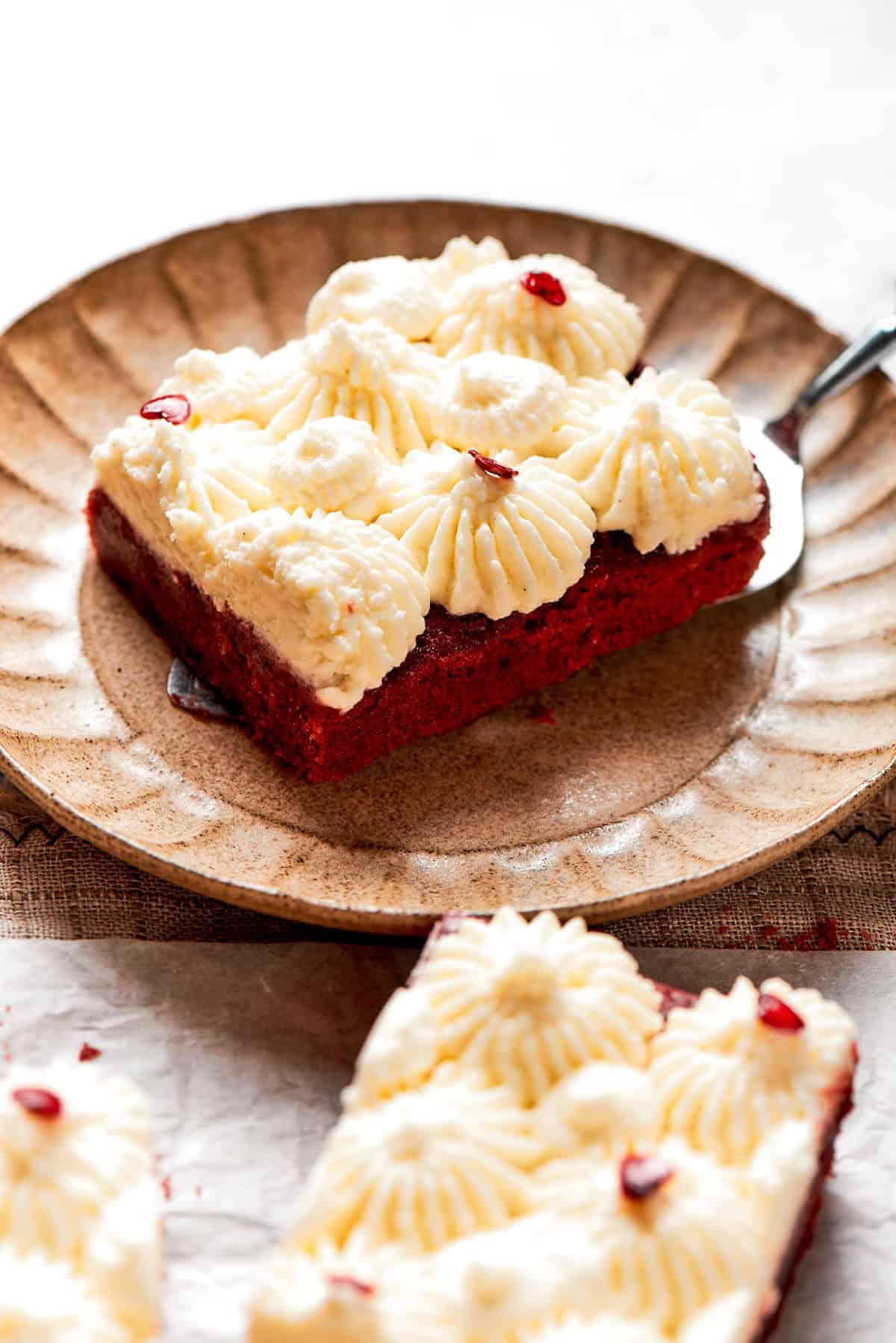 A red velvet brownie topped with frosting and served on a dessert plate.