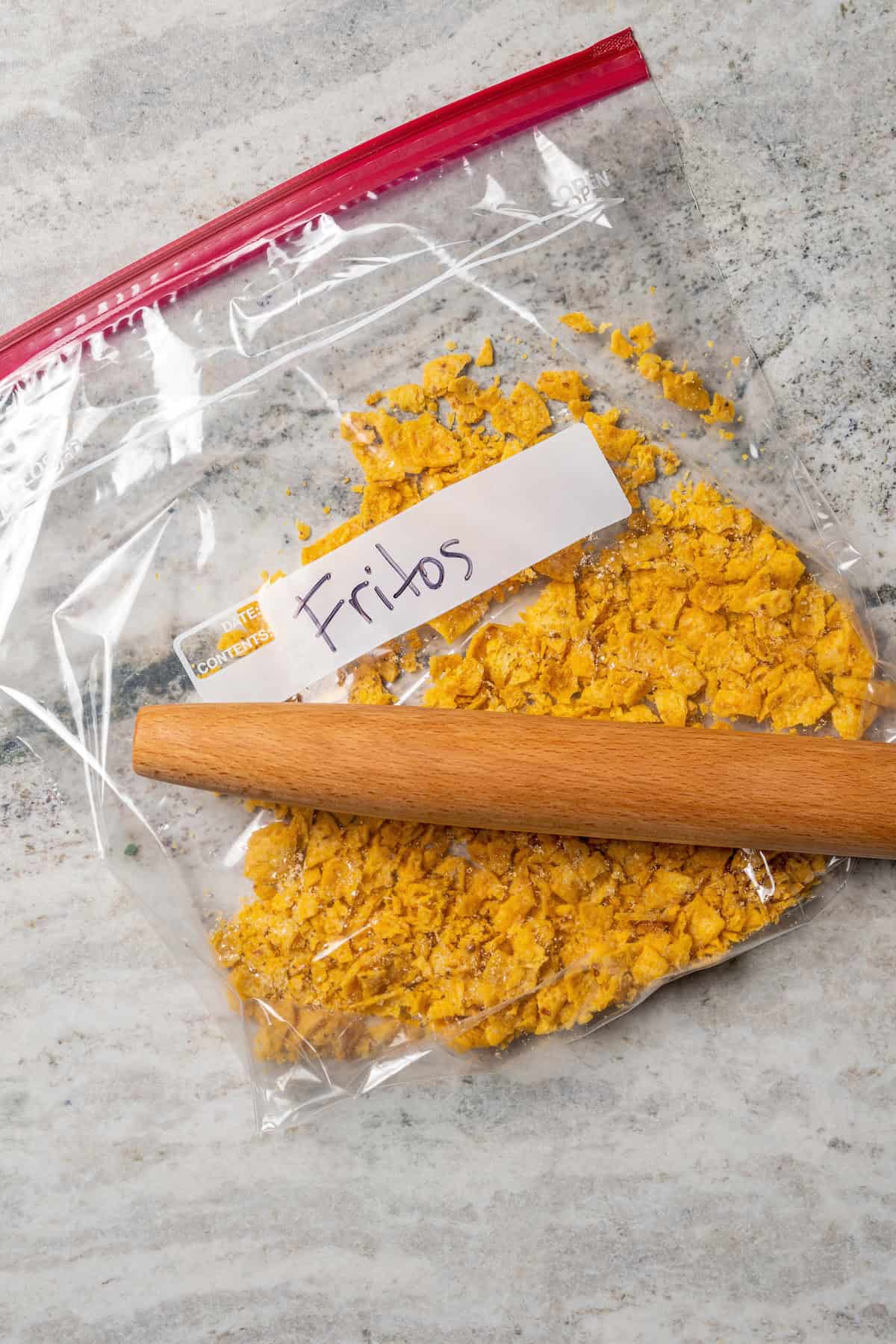 A wooden rolling pin resting on a resealable bag filled with crushed Fritos.