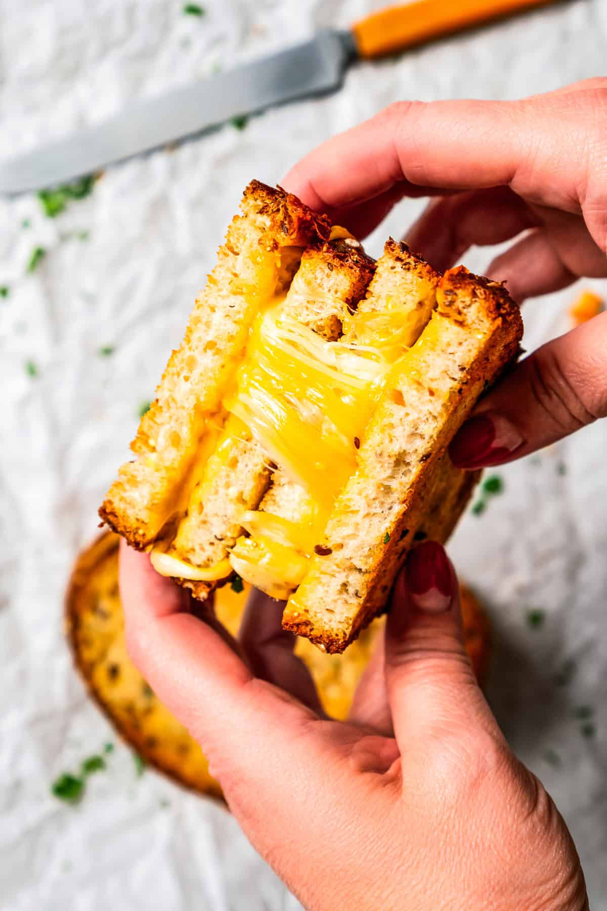 Two hands holding up halves of a grilled cheese, showing the melty cheese.