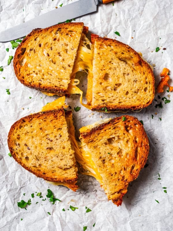 Two air fryer grilled cheese sandwiches cut in half on a sheet of parchment, pulled apart to reveal strings of melty cheese.