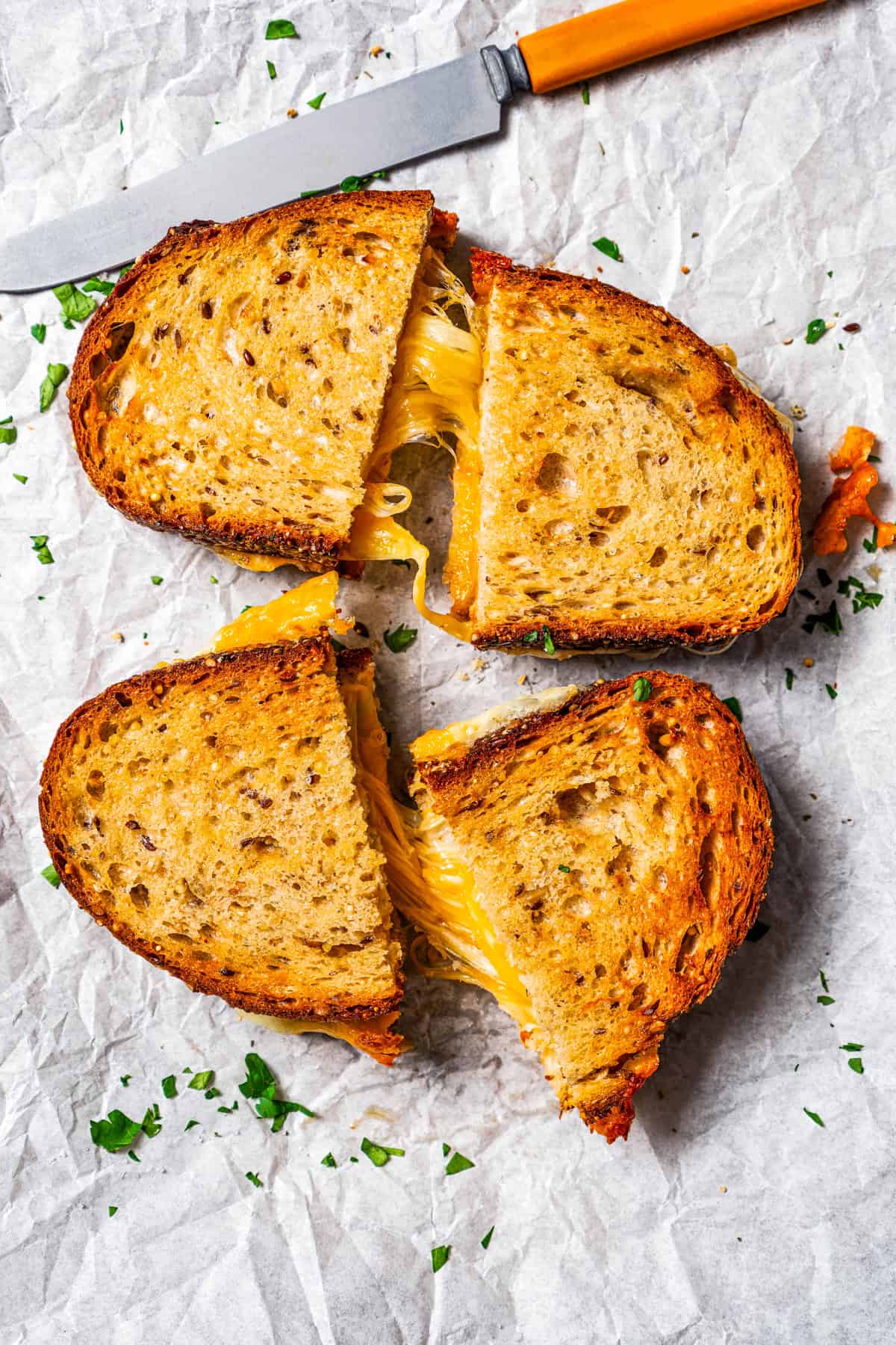 Two air fryer grilled cheese sandwiches cut in half on a sheet of parchment, pulled apart to reveal strings of melty cheese.