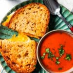 Grilled cheese sandwich served on a plate with a bowl of tomato soup.