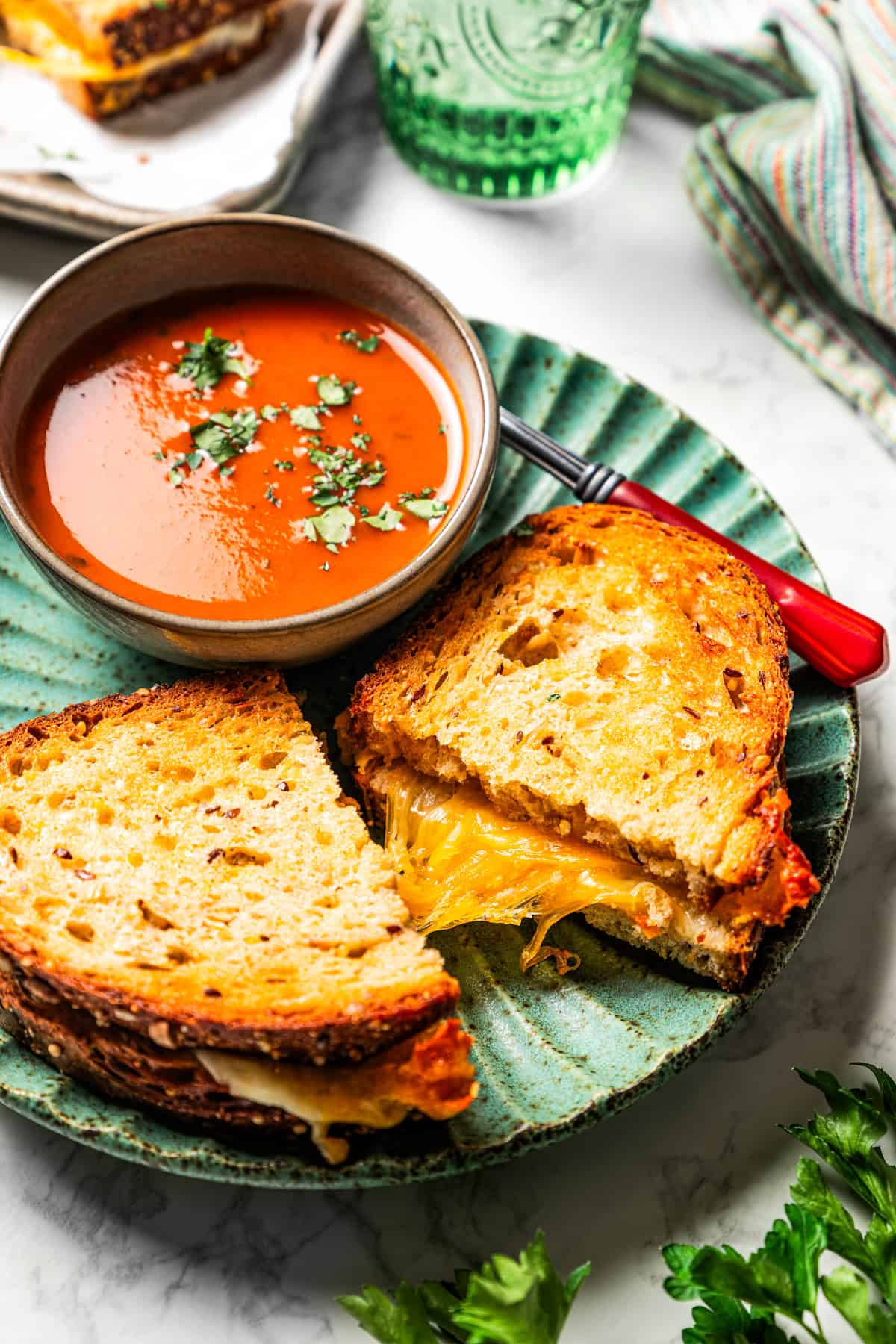 Air fryer grilled cheese cut in half next to a bowl of tomato soup and served on a green plate.