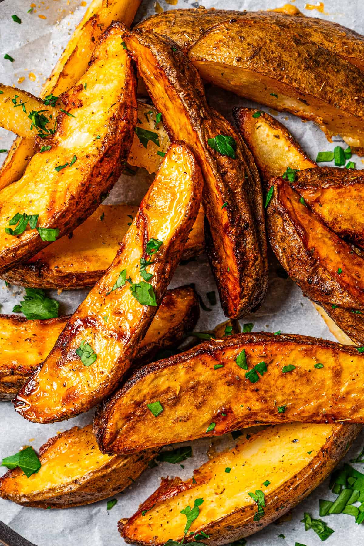 Air Fryer Potato Wedges A close-up of crispy potato wedges served on a surface lined with parchment paper.