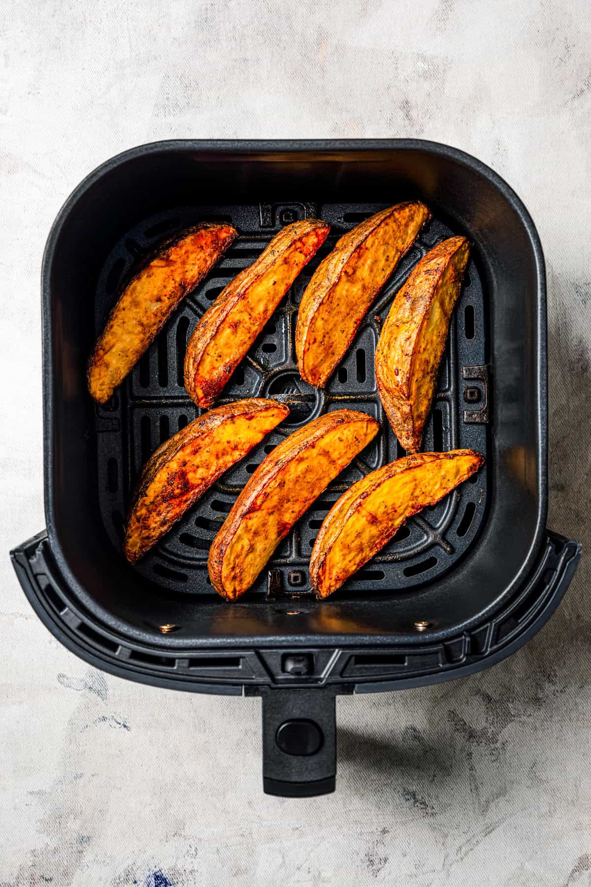 Potato wedges in an air fryer basket.