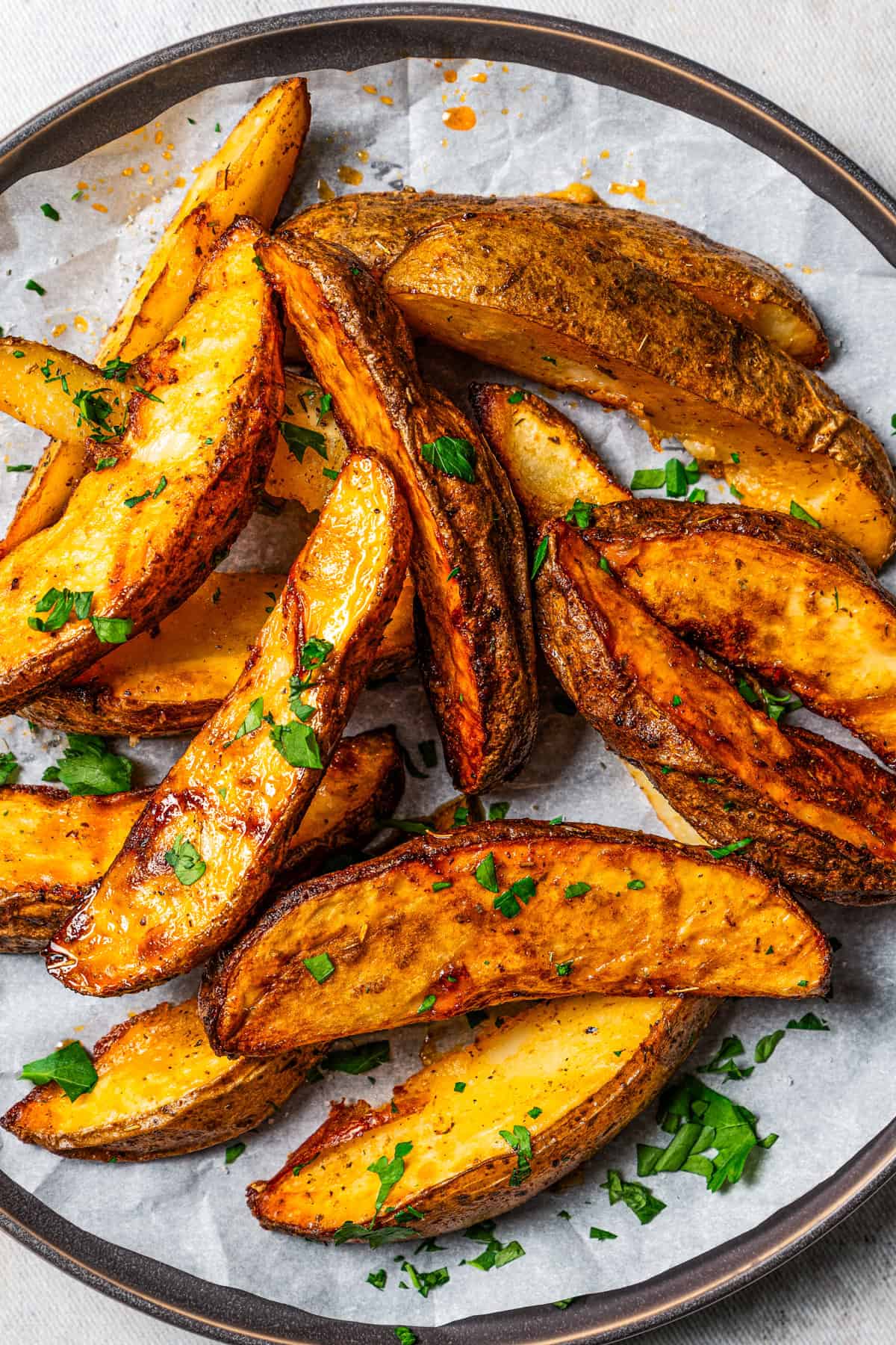 Air fryer potato wedges garnished with fresh parsley and arranged on a parchment-lined plate.