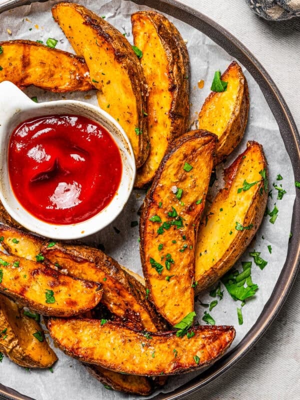 A wide shot of a plate filled with air fried potato wedges and a small bowl of ketchup.