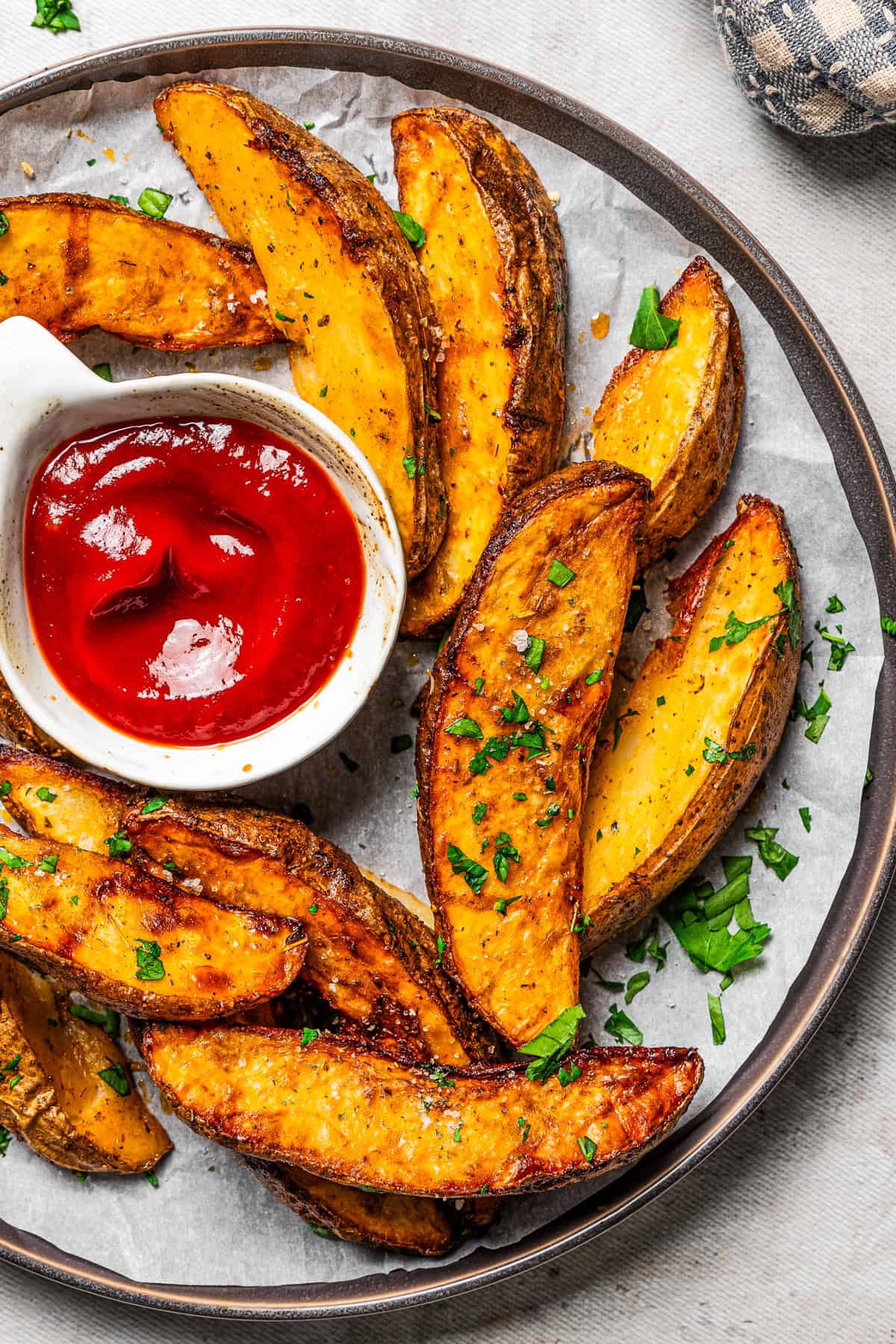 A wide shot of a plate filled with air fried potato wedges and a small bowl of ketchup.