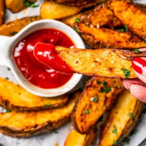 A hand holding a potato wedge dipped in ketchup.