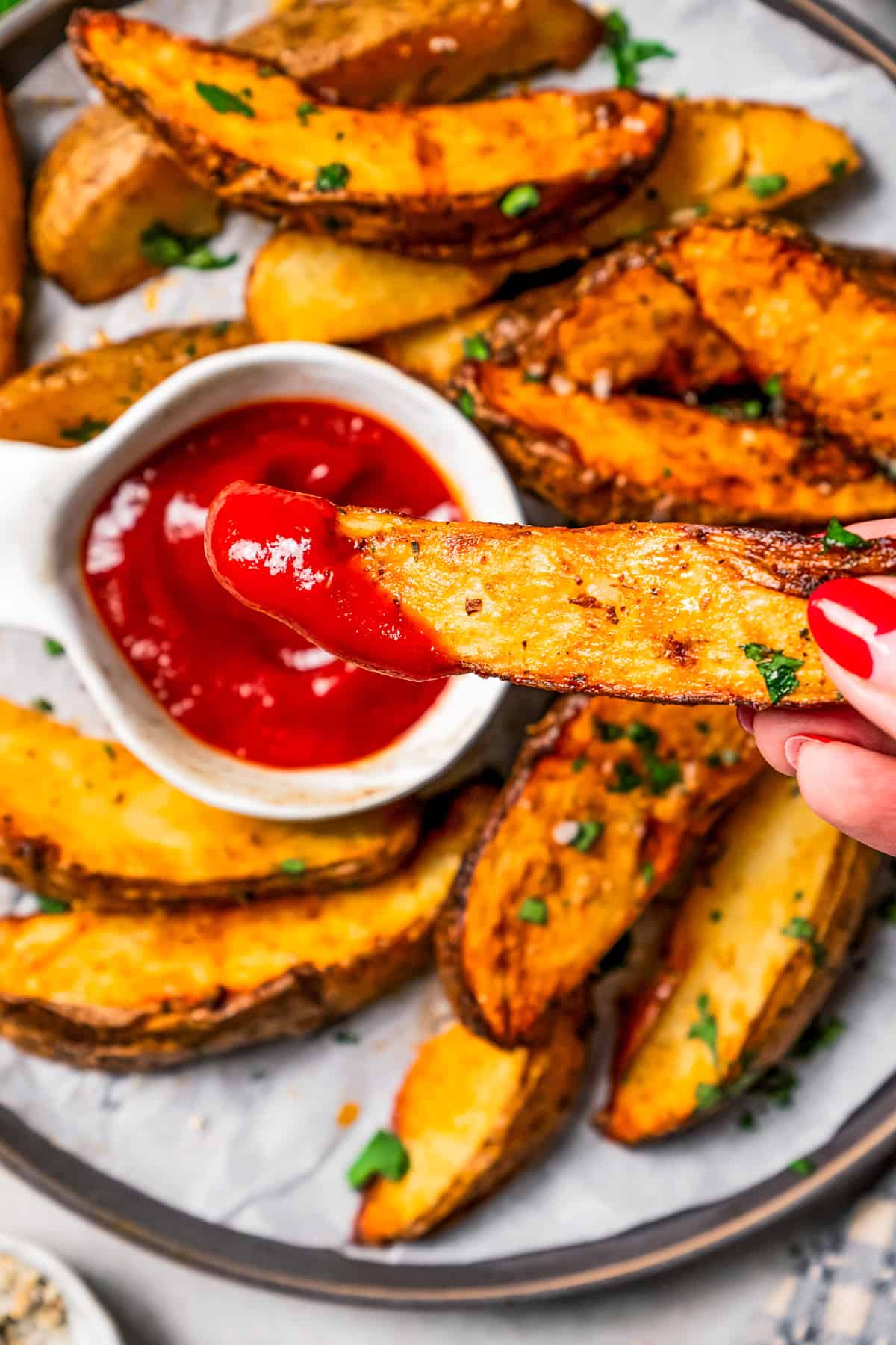 A hand holding a potato wedge dipped in ketchup.