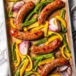 Baked Italian sausage with bell peppers and onions on a baking sheet.