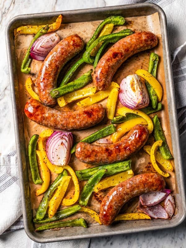 Baked Italian sausage with bell peppers and onions on a baking sheet.