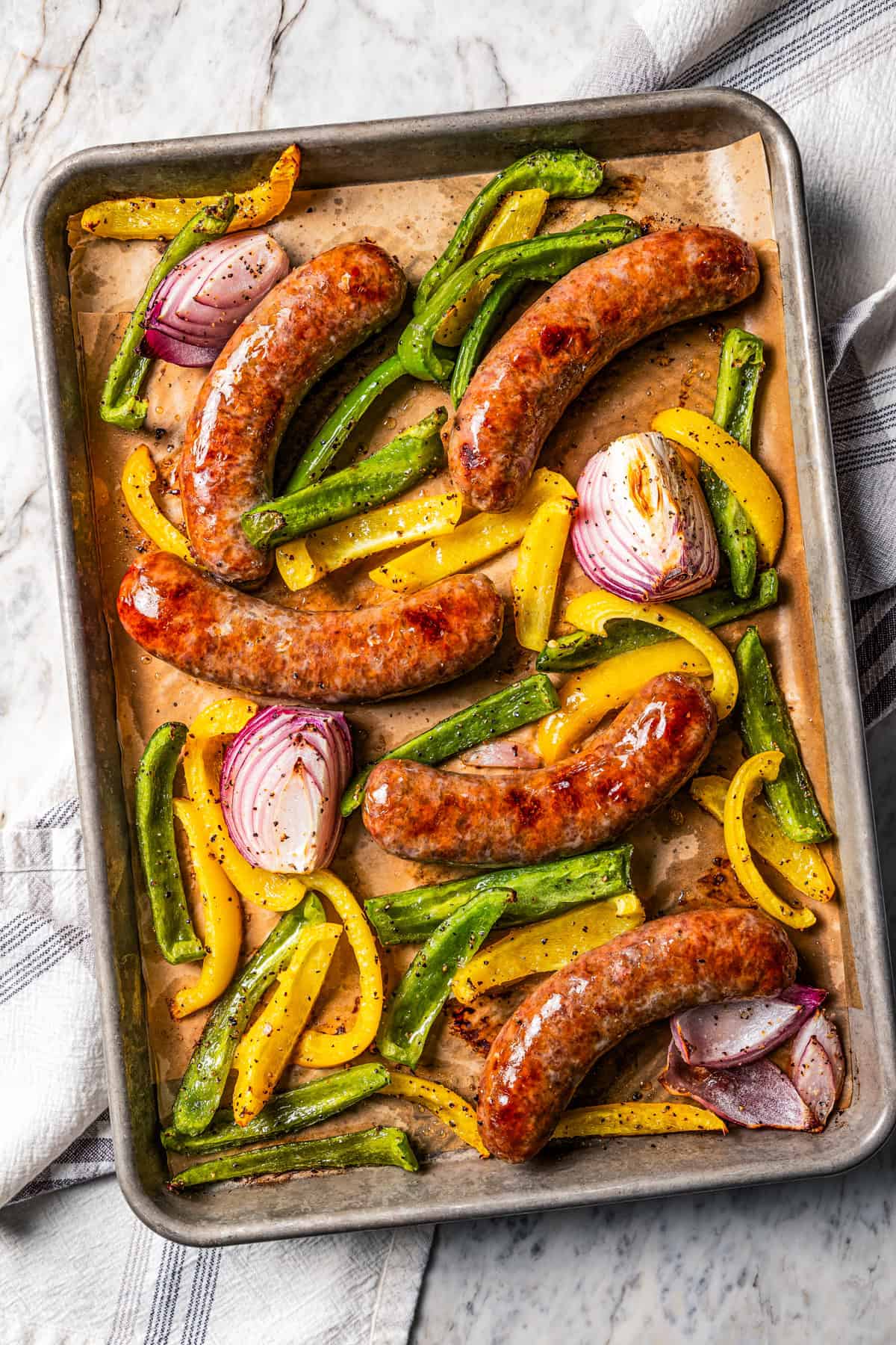 Baked Italian sausage with bell peppers and onions on a baking sheet.