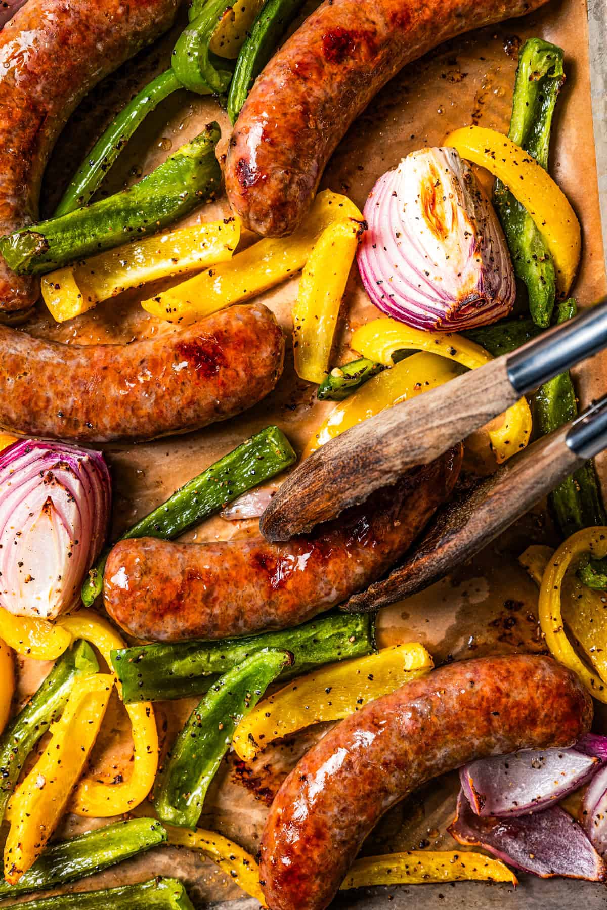 Tongs turning over Italian sausage in casings.