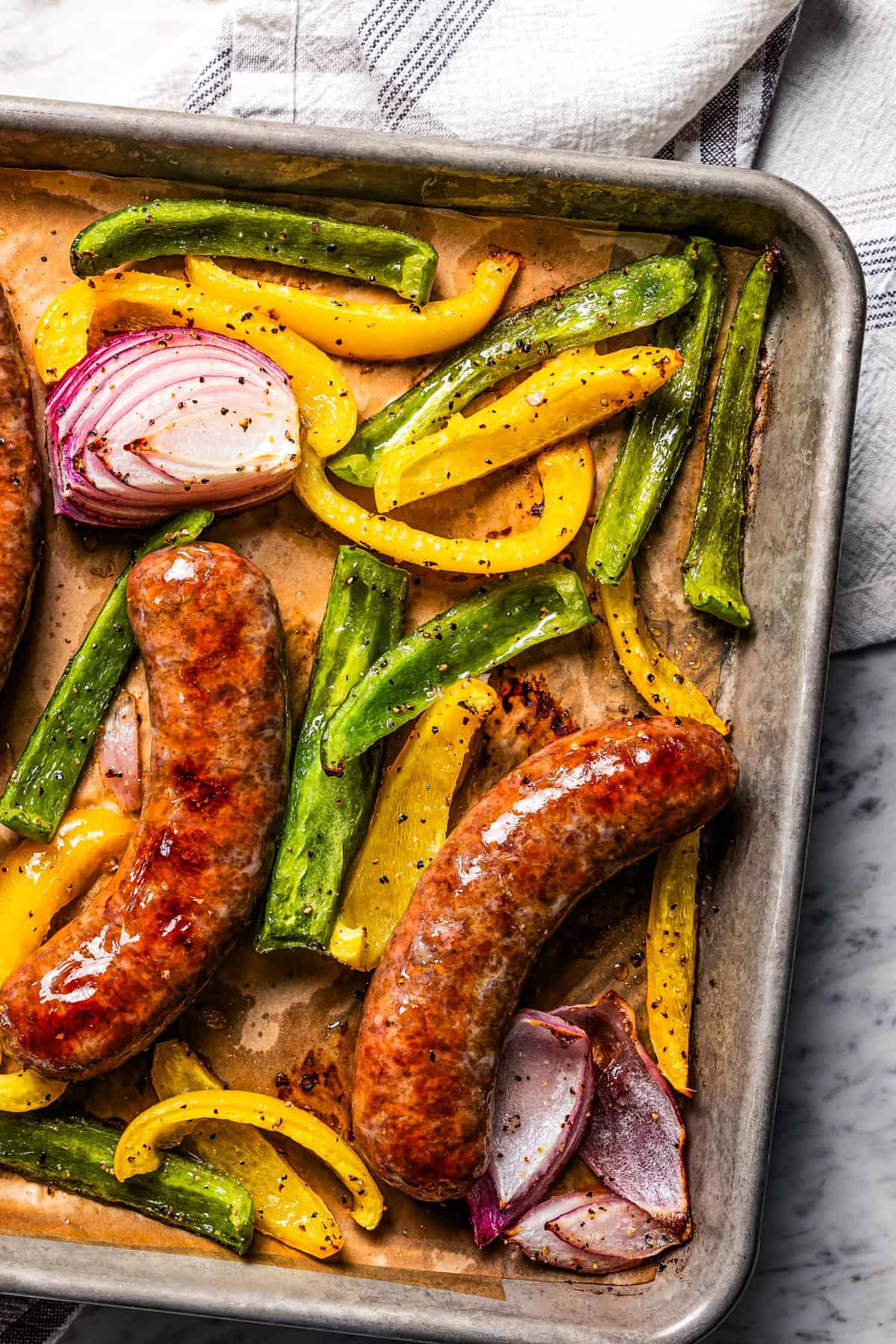 A sheet pan of baked sausage with peppers and onions.